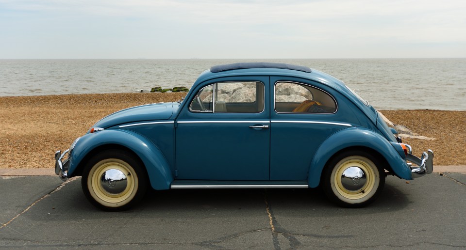 Blue Volkswagen Beetle parked by the ocean.