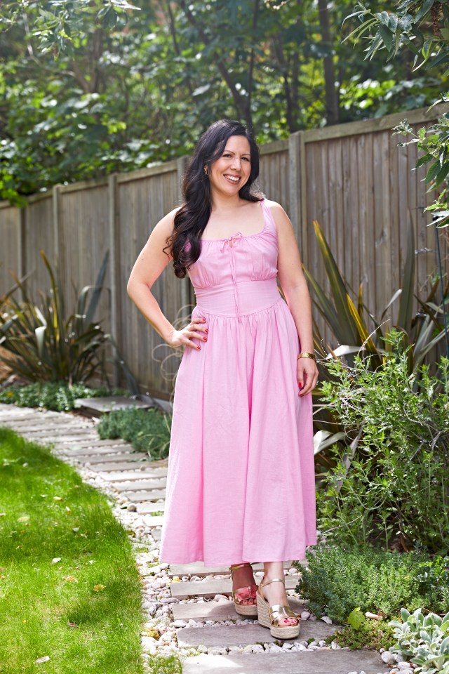 Woman in pink dress standing on a garden path.