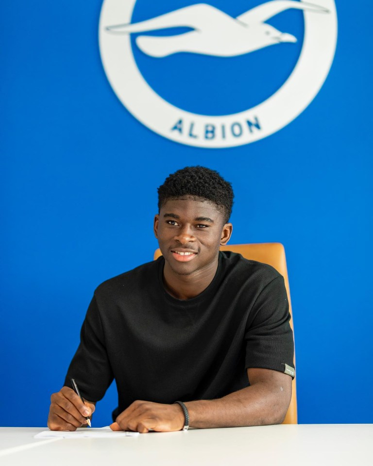 A young man signing a document at a table, with the Brighton & Hove Albion logo in the background.