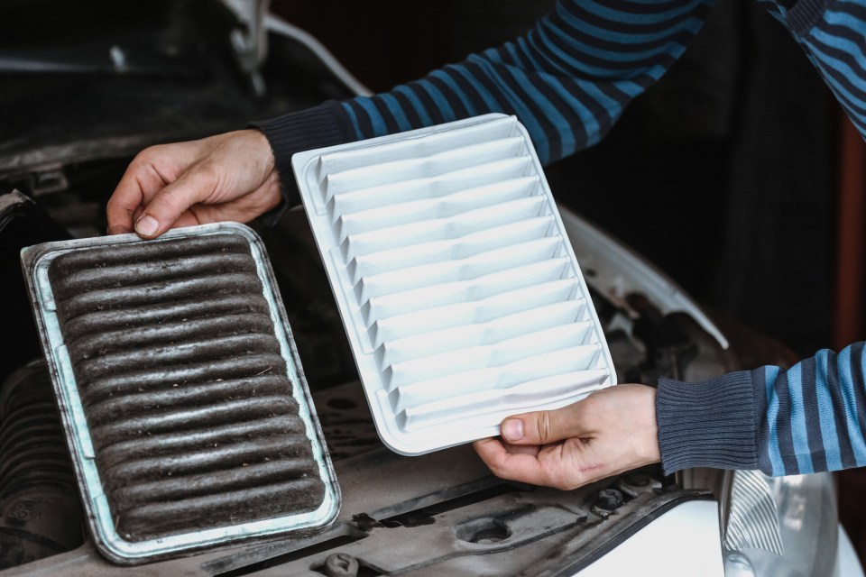 A person replacing a dirty car air filter with a new one.