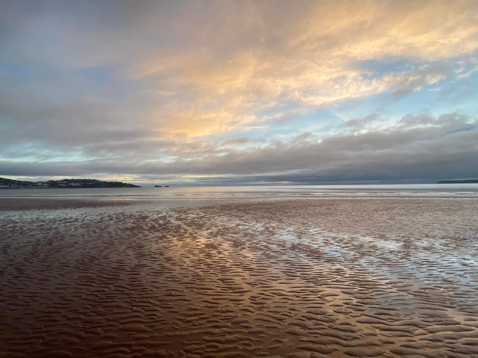 Sunset over a wet sandy beach.