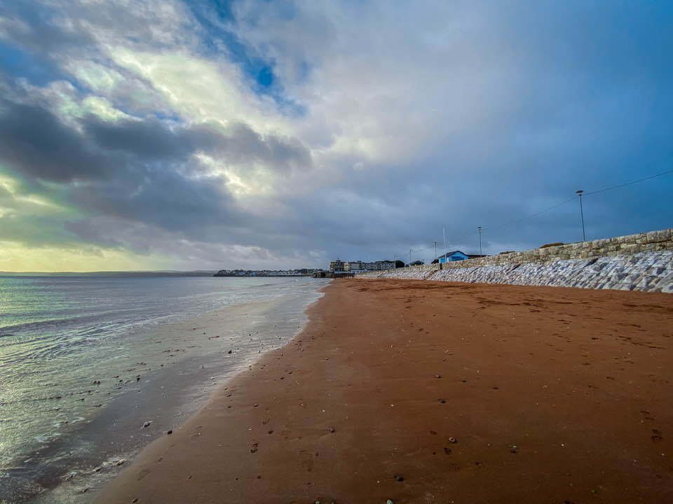 Sandy beach with ocean and cloudy sky.