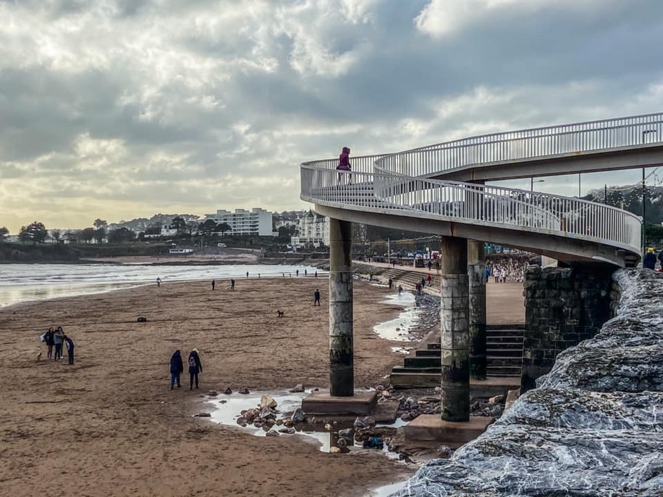 Elevated walkway over a beach with people walking on the sand.