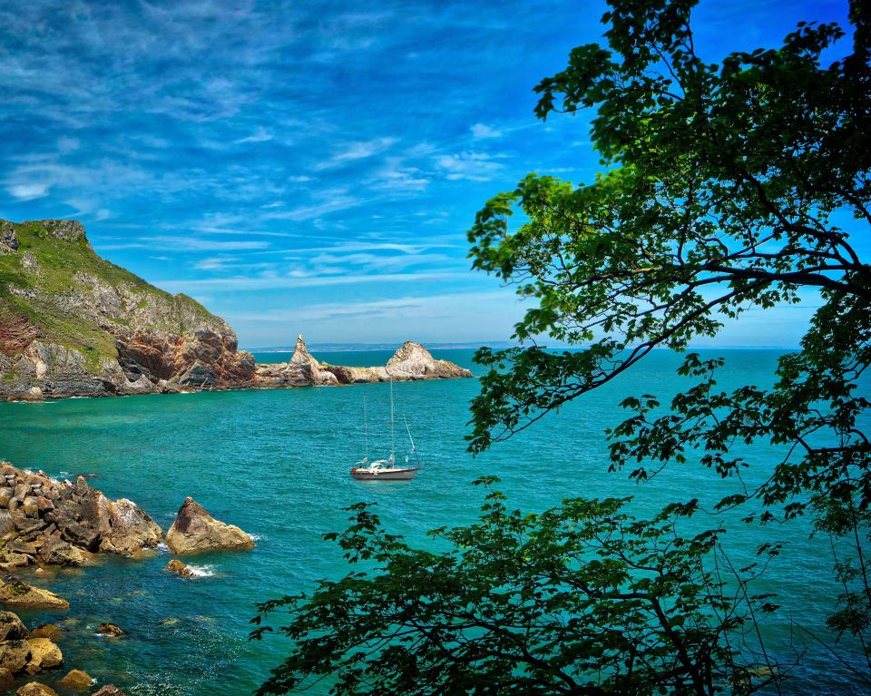 Sailboat in a cove near rocky cliffs.