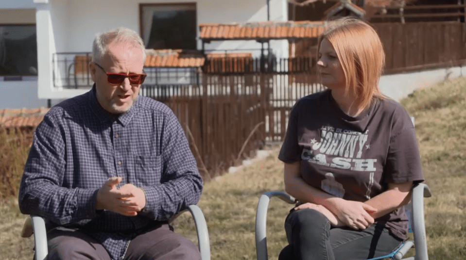 Two people sitting outdoors in chairs, talking.