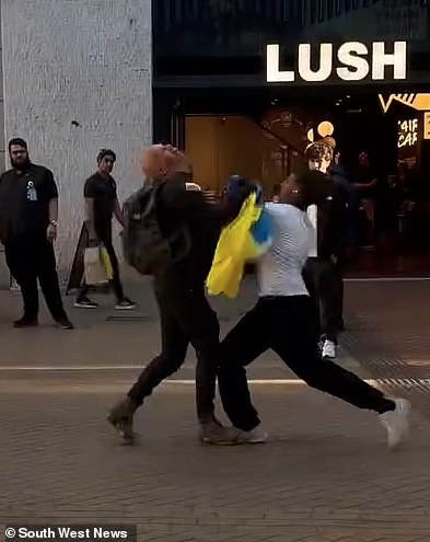 The man, clutching a Ukrainian flag, squared up towards another man wearing a white t-shirt before being stopped in his tracks by the powerful swing