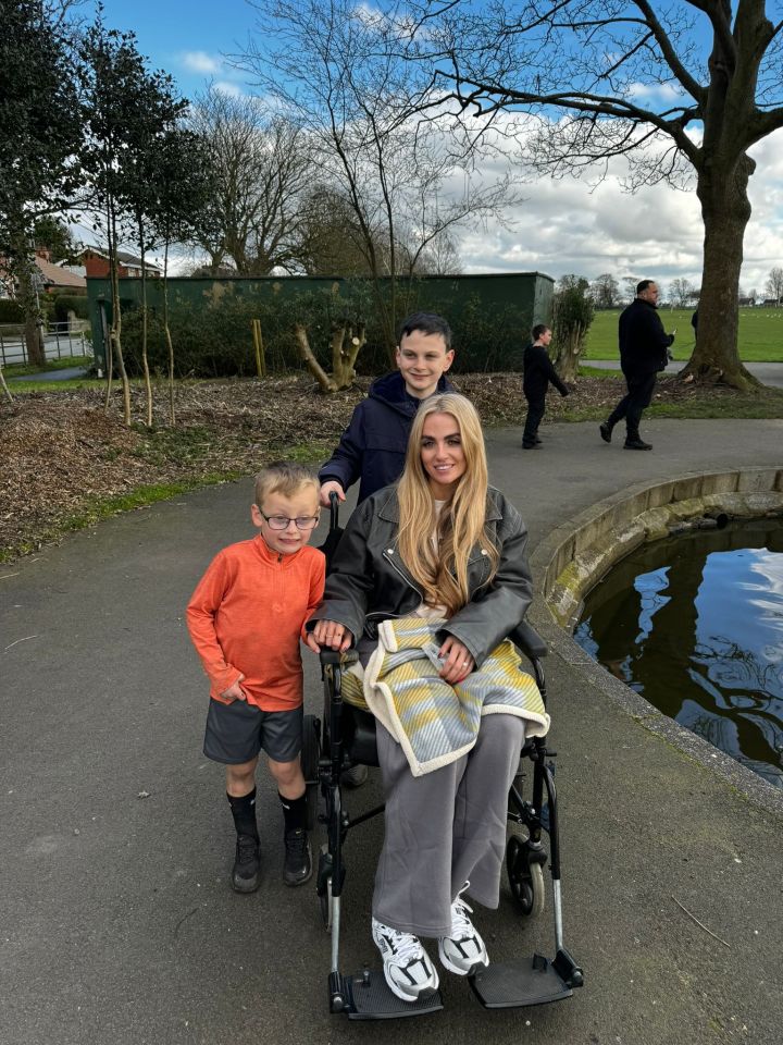 Woman in a wheelchair with two boys in a park.