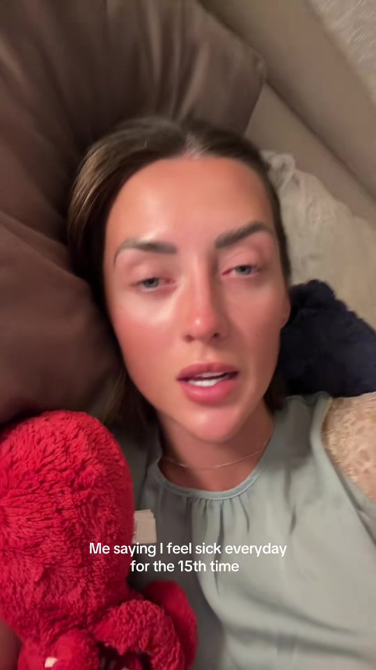A woman lying in bed looking unwell, holding a red plush octopus.  Text overlay reads, "Me saying I feel sick everyday for the 15th time".