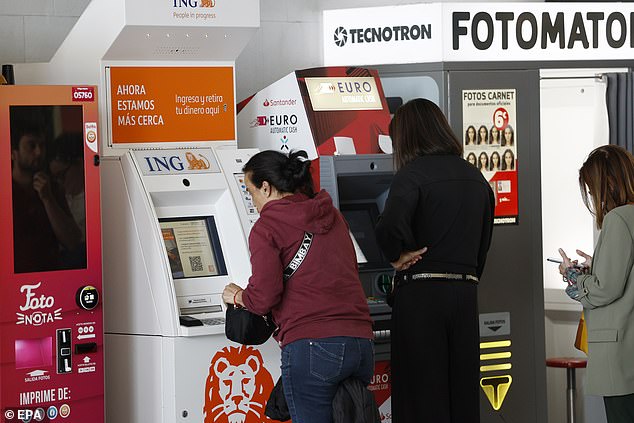 Several people get money out of several ATMs at the access of a subway station during a blackout hit Spain and Portugal in Madrid