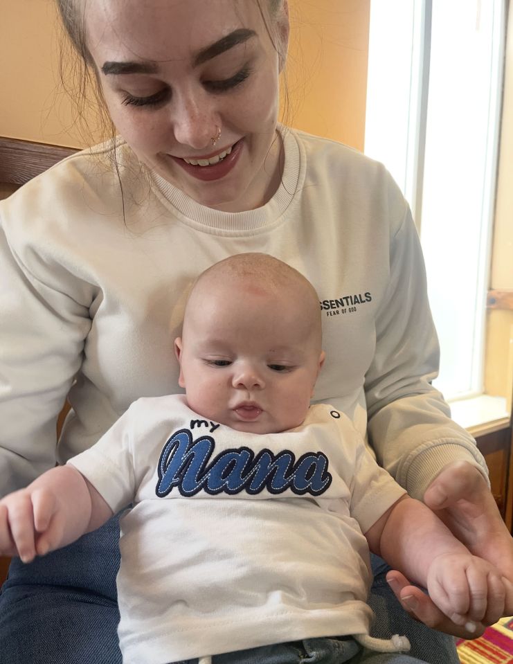 A young woman holding her baby, who is wearing a shirt that says "My Nana".