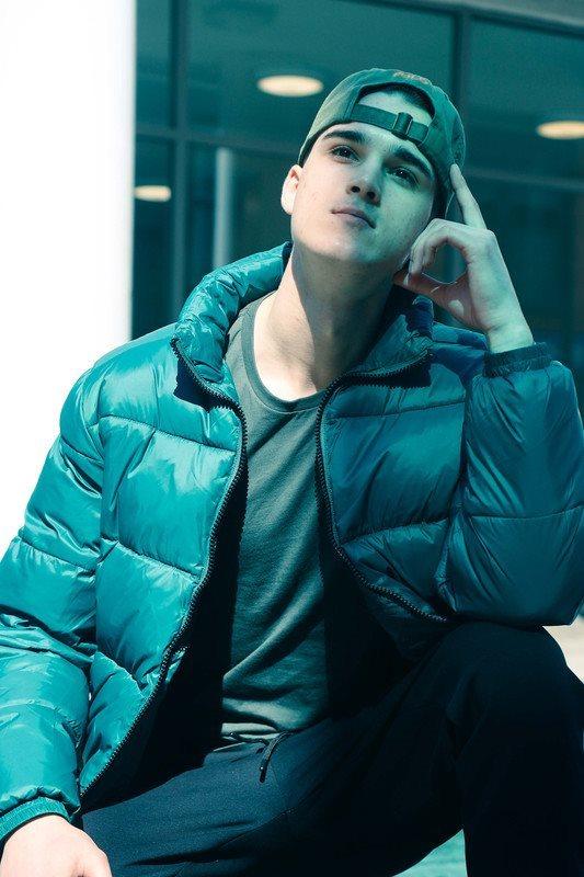Portrait of a young man in a teal puffer jacket.
