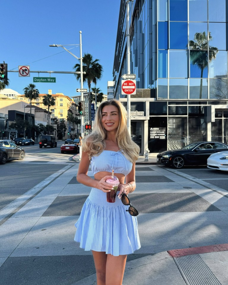 Woman in blue striped crop top and skirt holding a drink on a city street.