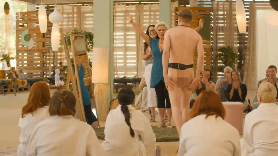 A nude man walks past a group of women in bathrobes.