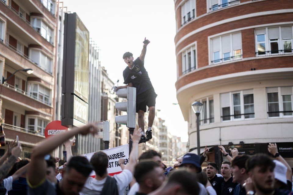 Tottenham Hotspur fan standing atop a traffic light, celebrating amidst a crowd of supporters.