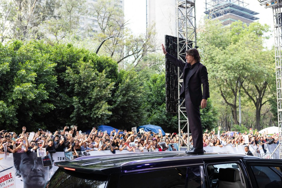 Tom Cruise waving to fans from a car at a Mission: Impossible premiere.