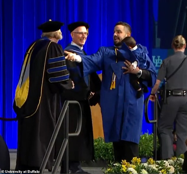 Clearly a bit disheveled by the time he reached the stage, the father picked up his dropped cap and made his way to shake hands with officials - his son still in his arms, fittingly dressed in a matching blue cap and gown