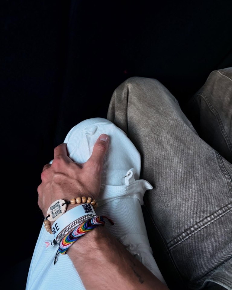 Person's hand resting on another person's lap, wearing several bracelets.