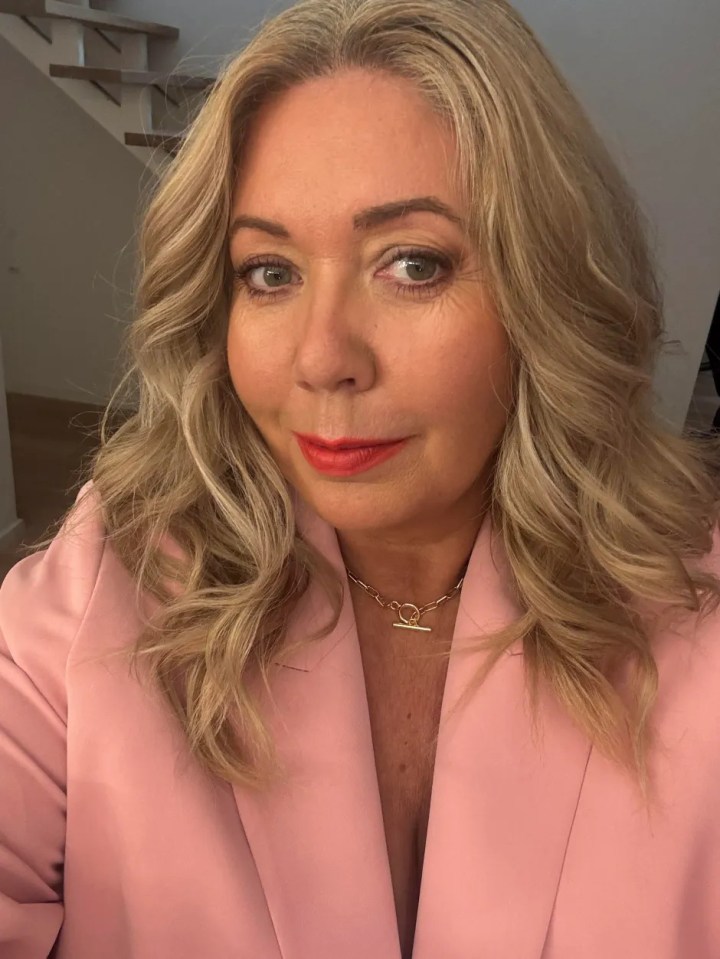 Woman in pink blazer and gold necklace.