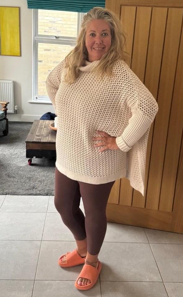 Woman in a cream sweater and maroon leggings standing in her home.