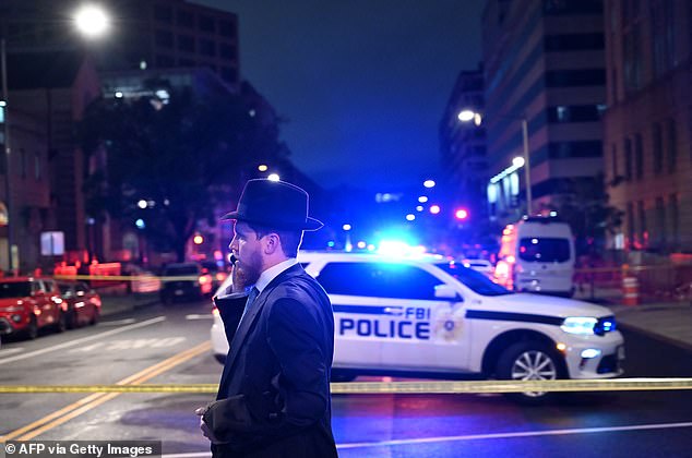 A man, standing behind police tape, talks on his cell phone outside the Capital Jewish Museum following the shooting