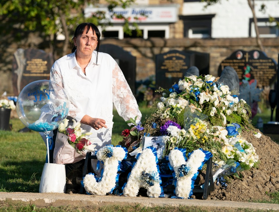 Woman mourning at a gravesite with floral tributes spelling "JAY".