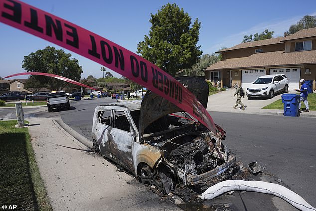 Police tape blows in the wind next to a burned vehicle after a small plane crashed into a San Diego neighborhood