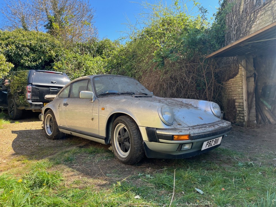 Dust-covered silver Porsche 911 Carrera in a yard.