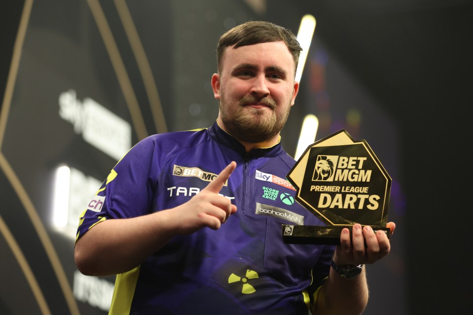 Luke Littler holding the BetMGM Premier League Darts trophy.