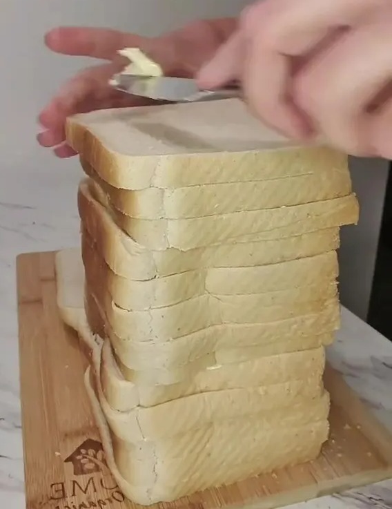 Butter being spread on a large stack of bread slices.