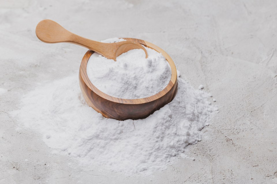 Baking soda in a wooden bowl with a wooden spoon.