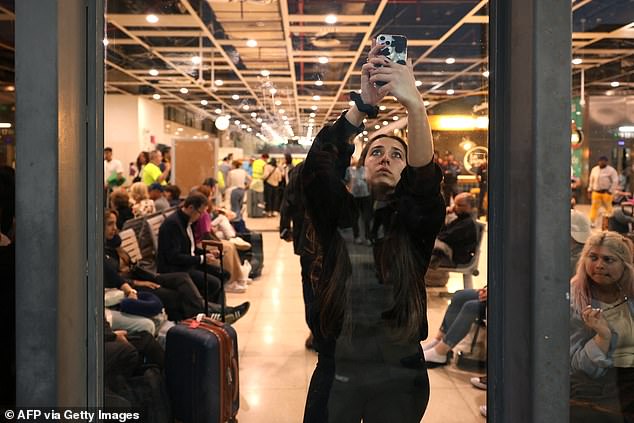 A traveller raise her phone up to catch network inside Barcelona-Sants rail station during a massive power cut affecting the entire Iberian peninsula and the south of France, in Barcelona on April 28, 2025