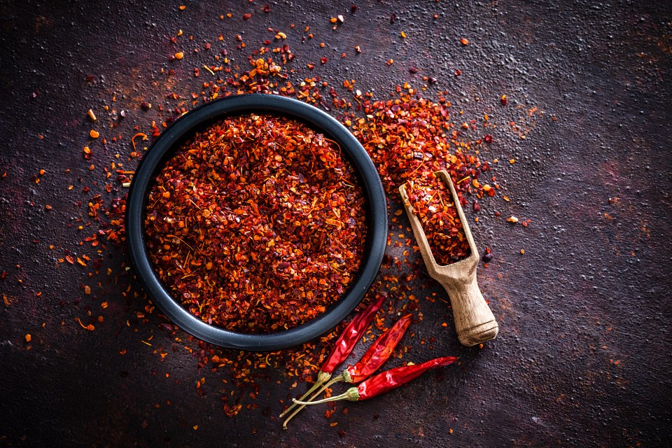 Crushed red pepper flakes in a black bowl with a wooden scoop and dried chilies.