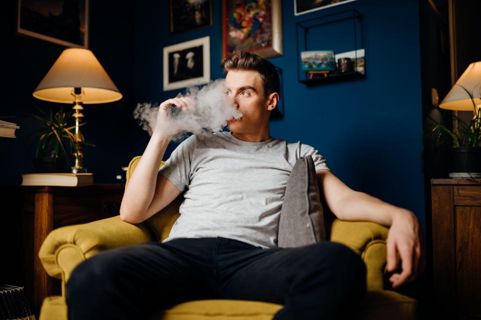 Young man vaping on a couch.