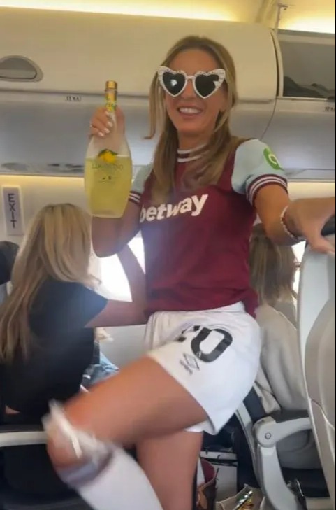 Dani Dyer on a plane holding a bottle of Limoncello while wearing a West Ham shirt.