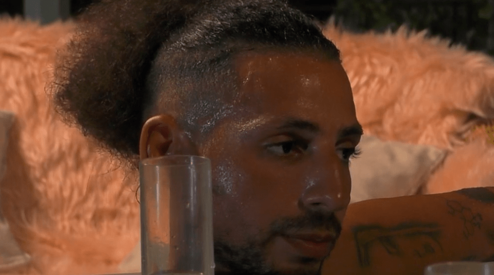 A sweaty man with a topknot looks pensively to his side.