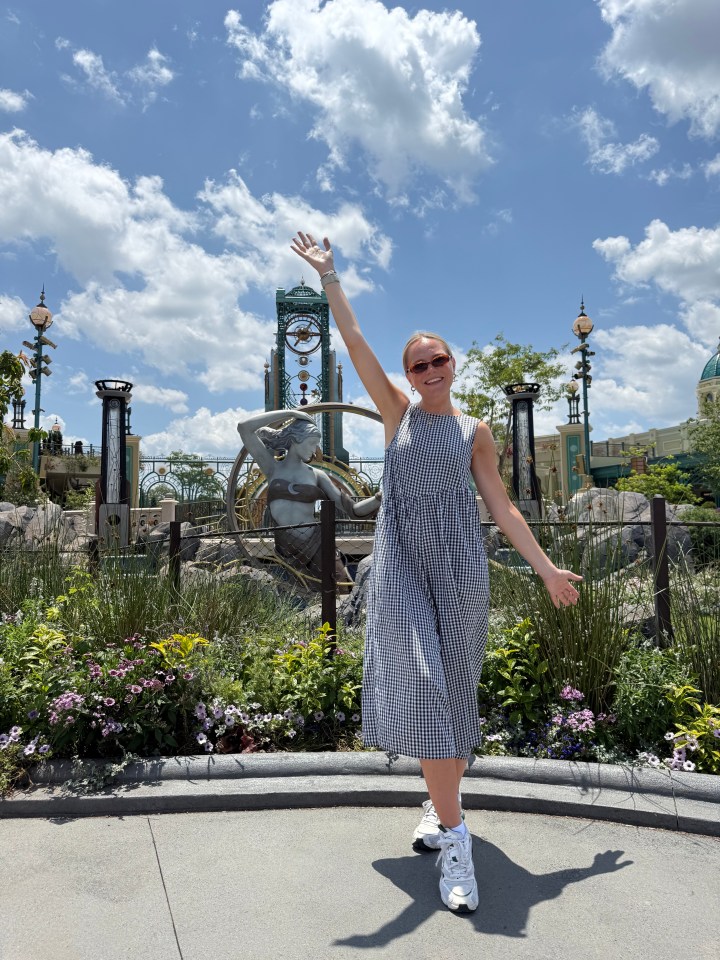 Woman in gingham dress poses in front of a fountain and clock tower.