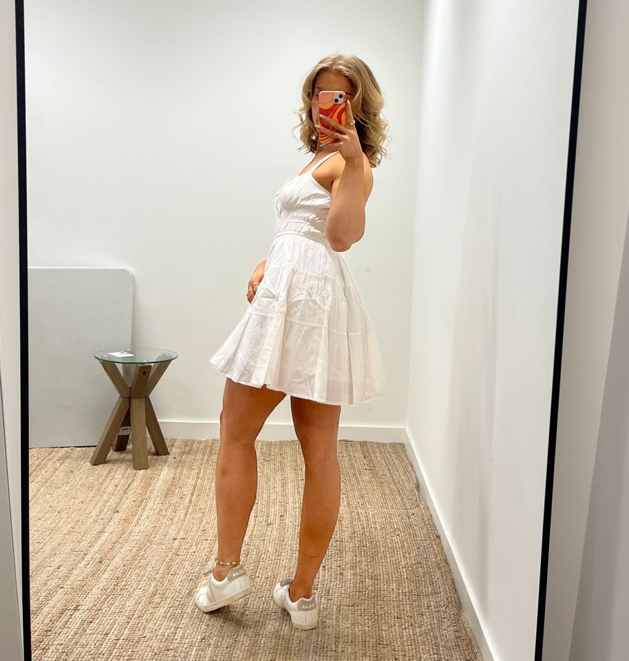 Woman in white dress taking a selfie in a mirror.