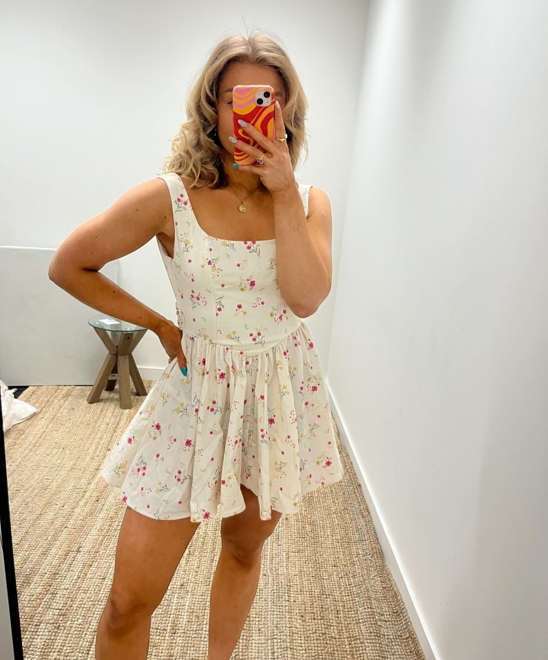 Woman in floral dress holding phone in front of mirror.