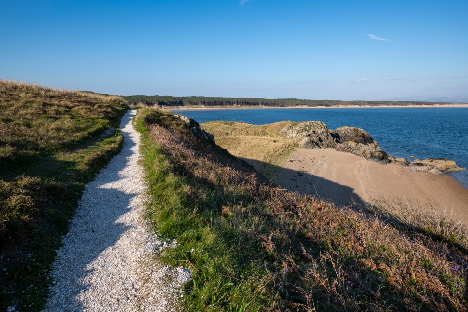 Coastal path overlooking a sandy beach and calm sea.
