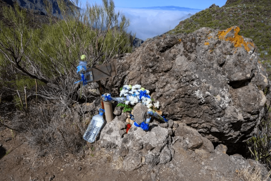 Memorial with flowers and water bottles near a rock.