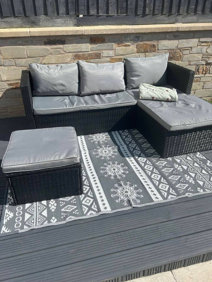 Rattan garden sofa set with gray cushions and patterned rug on a deck.
