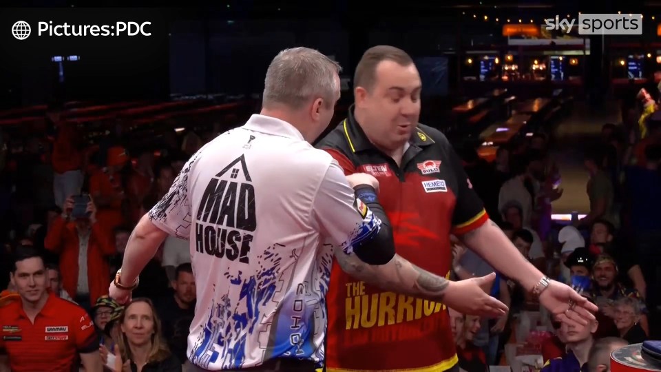 Two darts players on stage, appearing to argue.