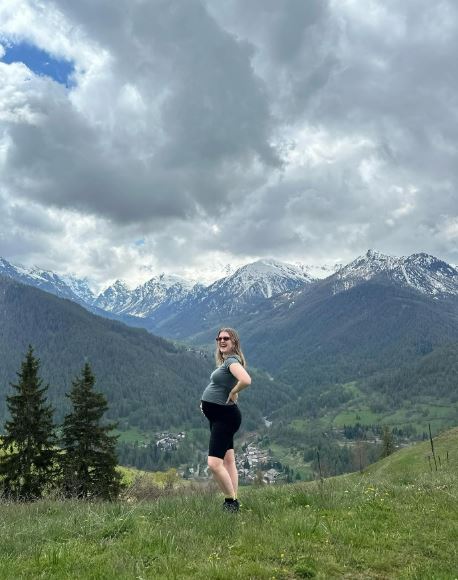 Pregnant woman standing in a mountain landscape.