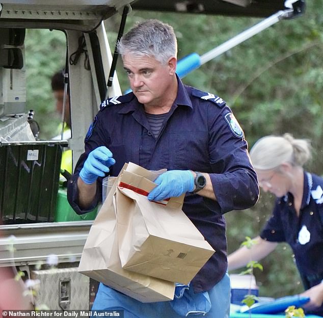 An officer is pictured carrying brown paper evidence bags at Good Night Scrub Park on Saturday as investigations into the missing 17-year-old continue