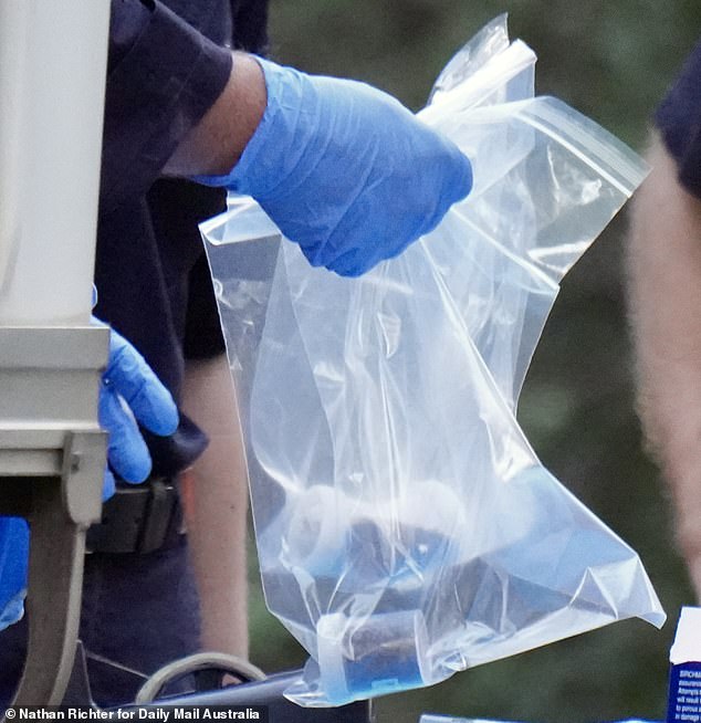 An officer is pictured carrying one of several plastic bags with sample jars full of soil