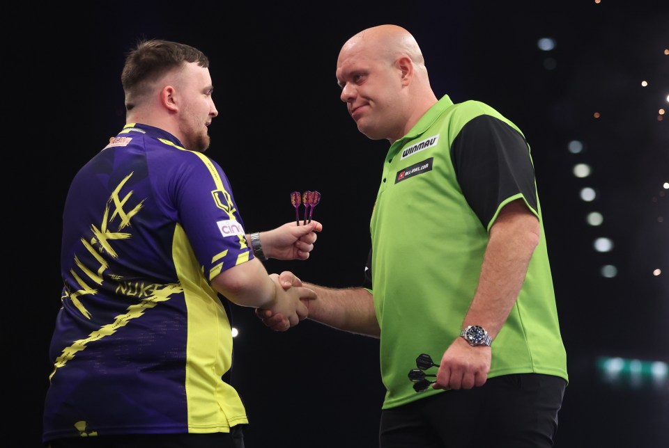 Luke Littler and Michael van Gerwen shaking hands at a darts match.