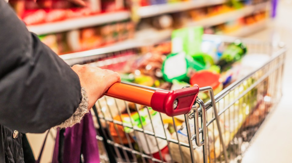 Person's hand on supermarket trolley handle, filled with groceries.