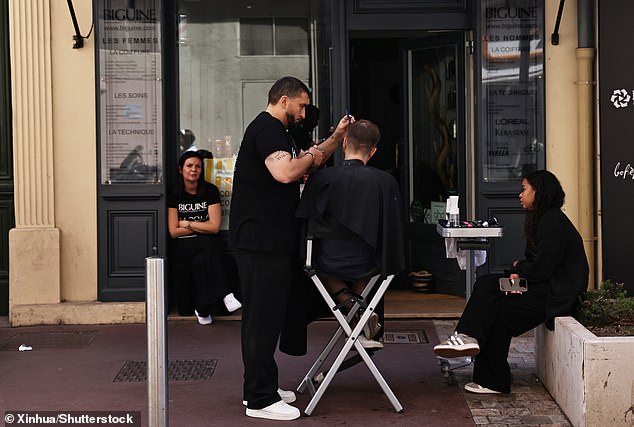 A barber gives a haircut to a customer outside a shop after a power outage in Cannes