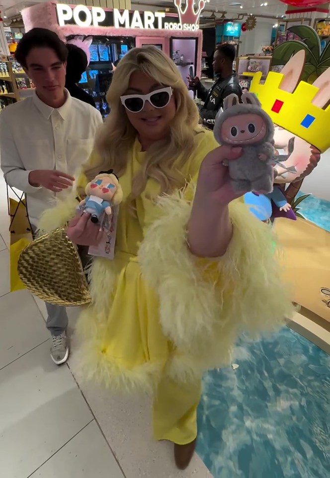 Gemma Collins in a yellow outfit at a Pop Mart store, holding Labubu toys.