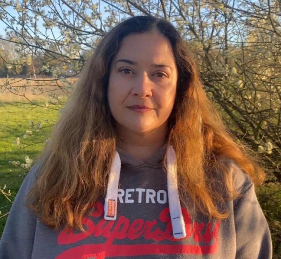 Woman with long brown hair wearing a gray hoodie outdoors in front of a flowering tree.